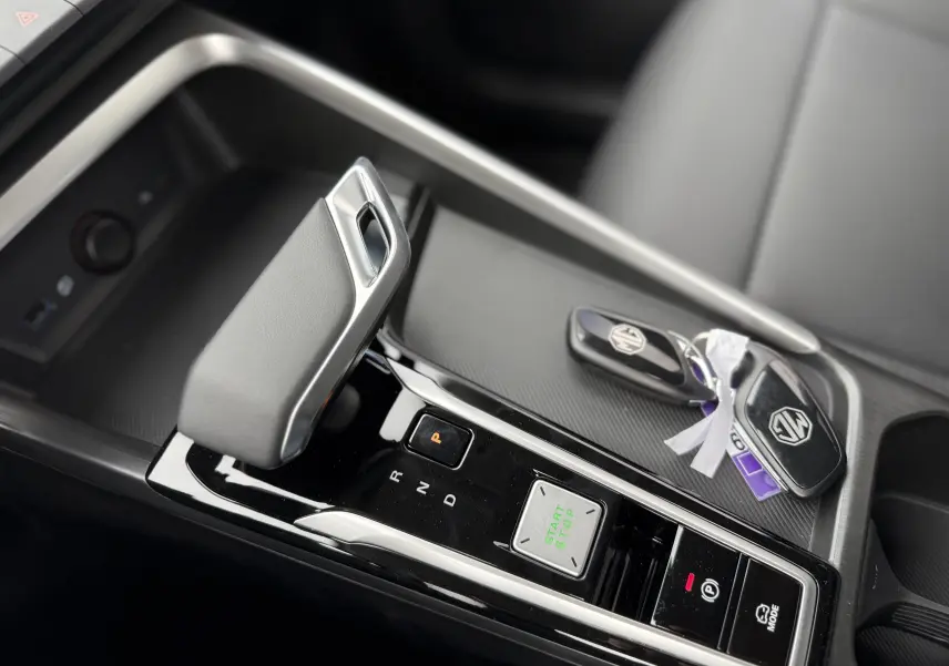 Gros plan sur la console centrale du MG ZS 1.5 Hybrid+ 197 Luxury, avec levier de vitesse et clés MG visibles.