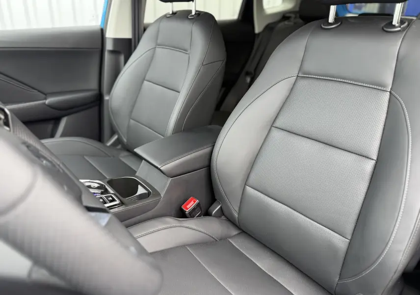 Vue intérieure rapprochée des sièges avant en cuir noir du MG MOTOR ZS 1.5 HYBRID+ 197 LUXURY, avec accoudoir central.