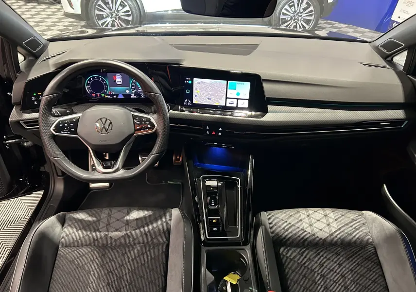Vue intérieure avant de la Volkswagen Golf VIII eTSI noire, avec tableau de bord numérique et écran tactile central.