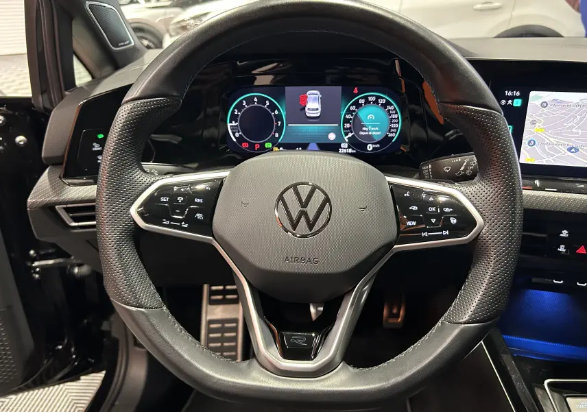 Vue intérieure centrée sur le volant en cuir perforé noir d'une Volkswagen Golf VIII eTSI 150CH avec tableau de bord numérique et écran tactile.