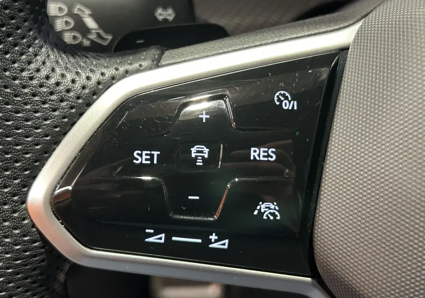 Gros plan sur les commandes de régulateur de vitesse au volant d'une Volkswagen Golf VIII eTSI noir métal.