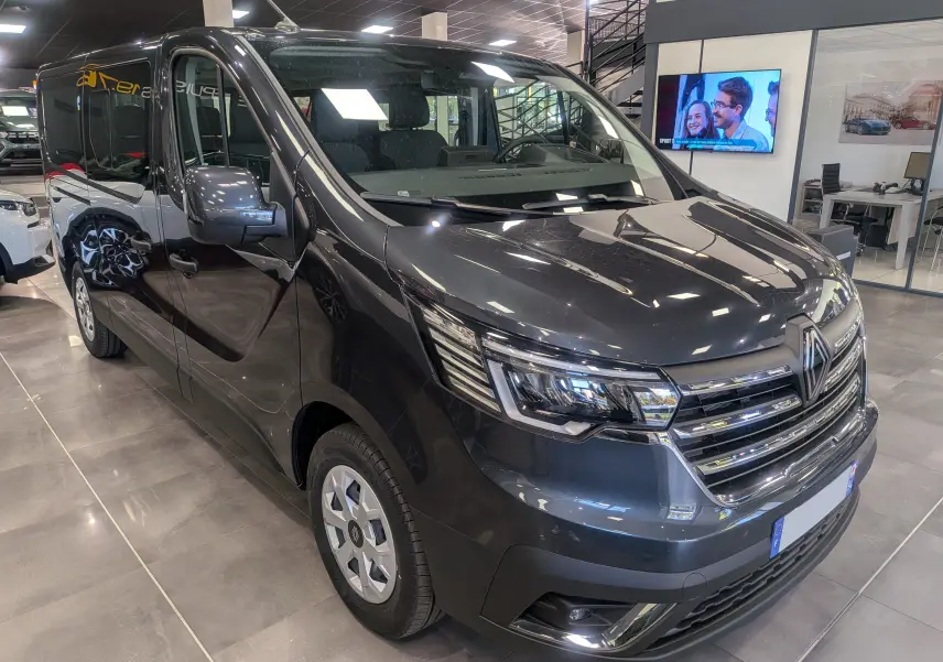 Renault Trafic Combi gris Comète vu en 3/4 avant droit dans un showroom lumineux avec détails chromés au niveau de la calandre.