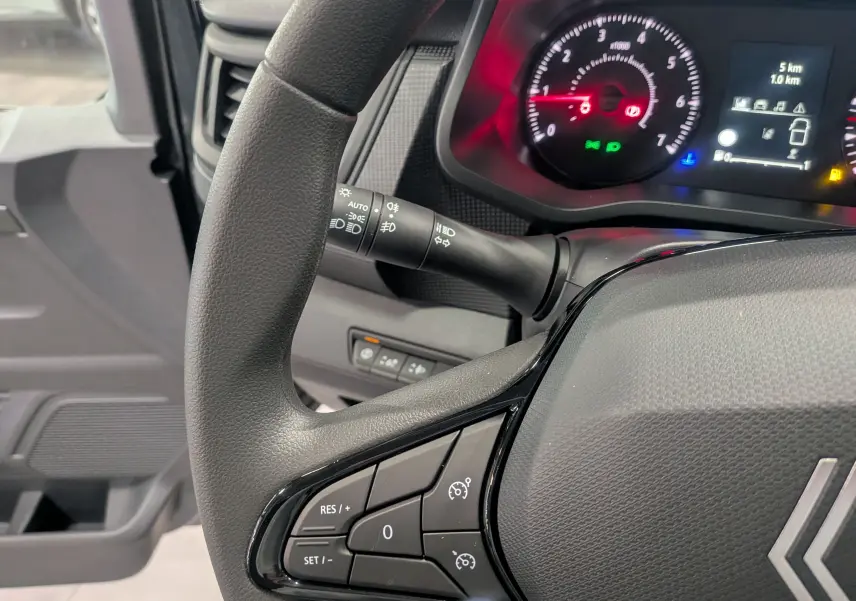 Gros plan sur le volant et le tableau de bord du Renault Trafic Combi 2025, avec commandes de régulateur de vitesse visibles.
