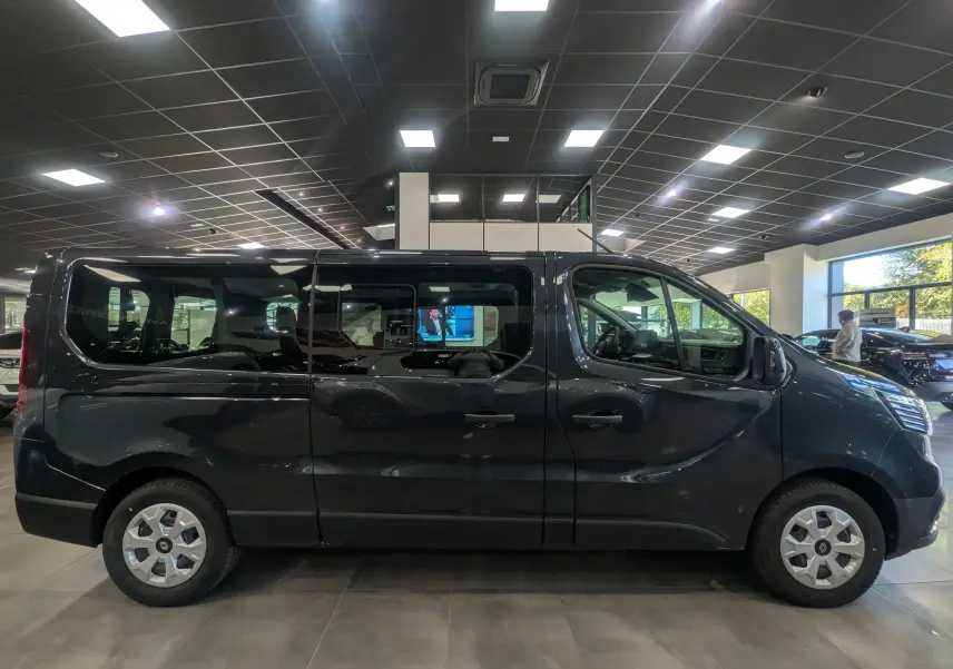 Vue latérale droite d'un Renault Trafic Combi 2025 gris Comète en showroom, soulignant ses grandes vitres teintées.