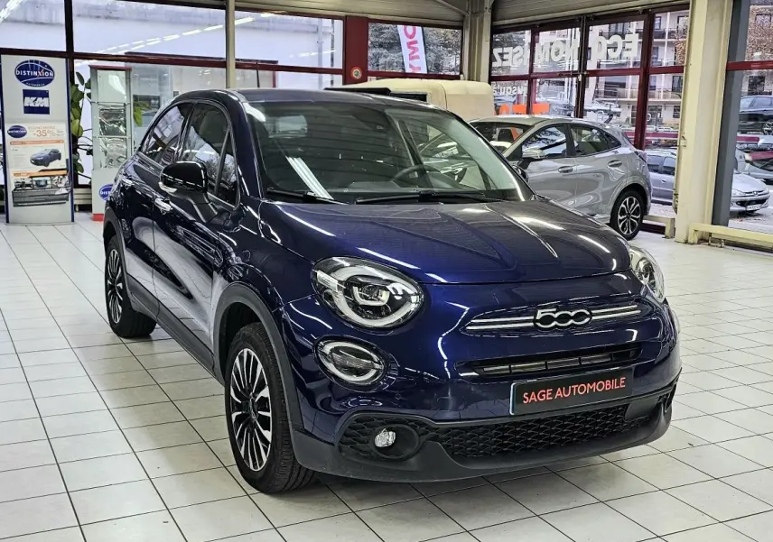 Vue 3/4 avant d'une FIAT 500X bleu nuit 2024 en hybride essence, avec calandre et phares ronds distinctifs en showroom.