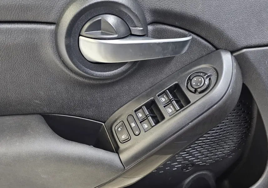 Gros plan sur la poignée intérieure et les commandes des vitres côté gauche d'une FIAT 500X Ph2 bleu 2024 hybride.
