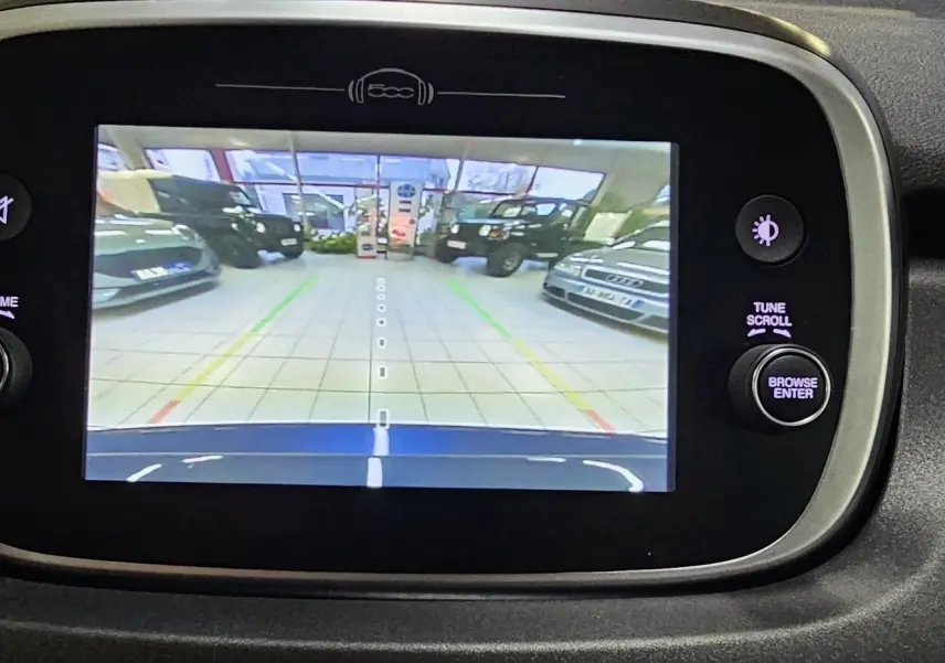 Écran central de la FIAT 500X 2024 montrant la caméra de recul avec vue sur le capot bleu et le garage en arrière-plan.