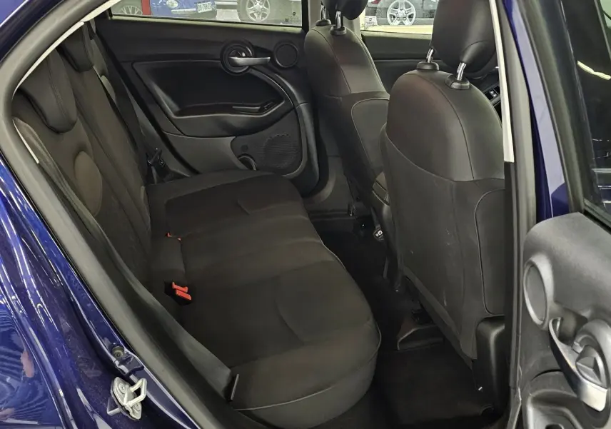 Vue intérieure arrière côté gauche d'une FIAT 500X 2024 bleue, montrant les sièges arrière noirs et la portière ouverte.