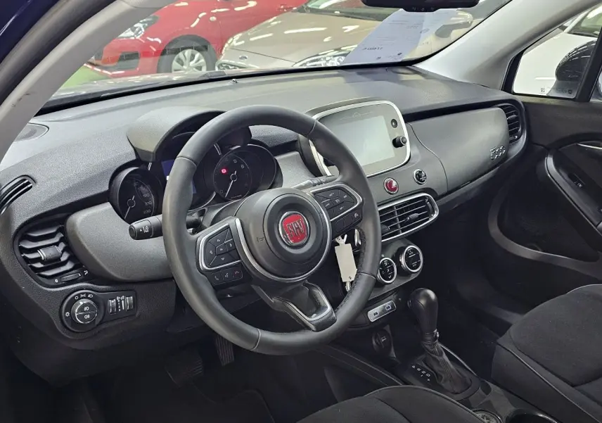 Intérieur du FIAT 500X 2024 vu côté conducteur, tableau de bord noir avec volant multifonction et écran tactile central.