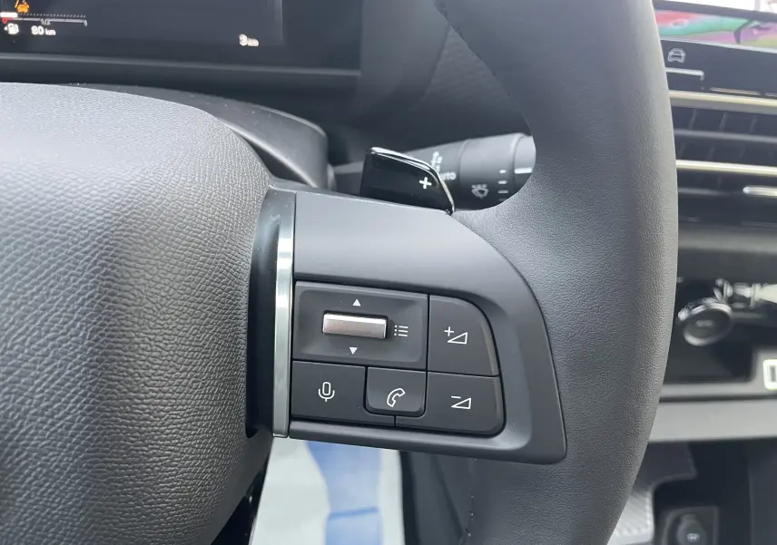 Gros plan sur les commandes au volant à gauche du Citroën C4 hybride 2025, intérieur noir avec boutons multifonctions.