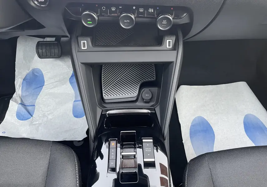 Vue intérieure centrée sur la console centrale noire brillante de la Citroën C4 hybride 2025 avec commandes climatisation et boîte auto.