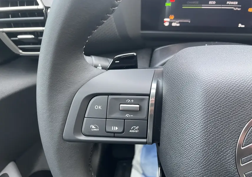 Gros plan sur les commandes à gauche du volant du Citroën C4 hybride 2025, avec boutons de limitation et assistance.