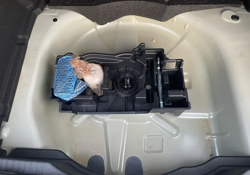 Vue plongeante sur le coffre ouvert de la Citroën C4 hybride blanche, montrant le rangement pour roue de secours et outils.