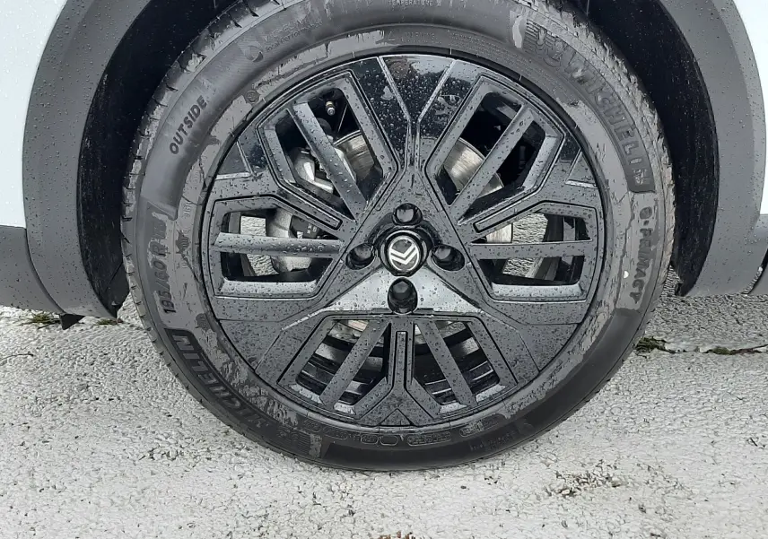 Gros plan sur la roue avant droite d'une Citroën C4 blanche, jante noire au design géométrique distinctif.