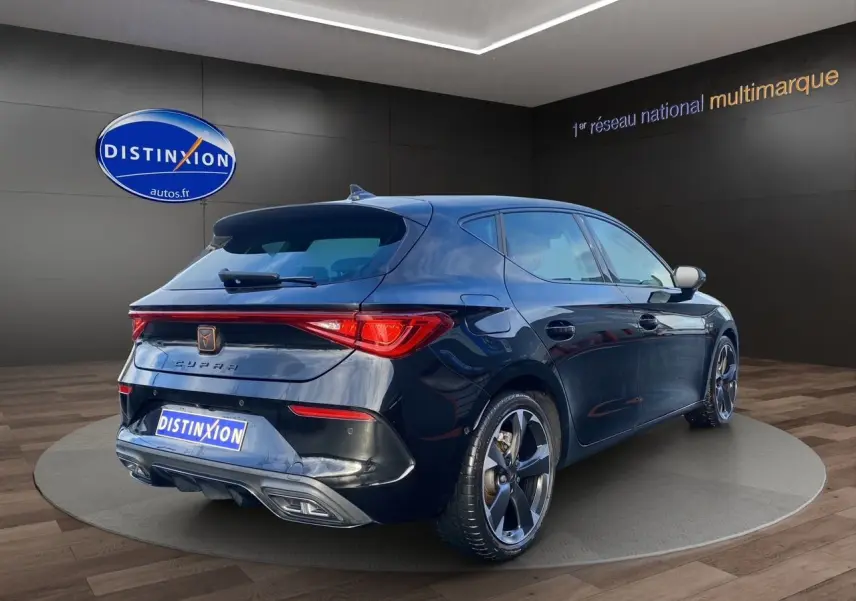 Vue 3/4 arrière droite d'une CUPRA Leon noire 2023 avec jantes alliage et feux arrière LED allumés.
