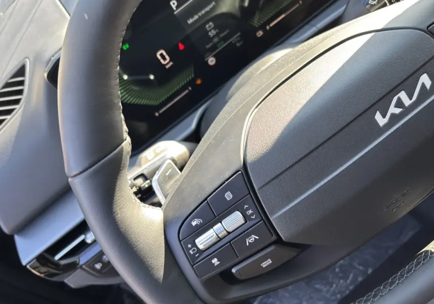 Gros plan sur le volant cuir multifonctions du Kia Sportage gris eclipse, avec commandes intégrées et tableau de bord numérique.