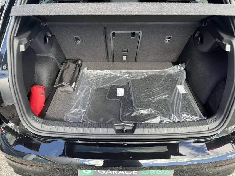 Vue du coffre ouvert d'une Volkswagen Golf noir Grenadilla métallisée, avec tapis de sol neufs emballés et rangement latéral visible.