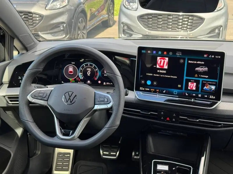 Vue intérieure du poste de conduite de la Volkswagen Golf noire, avec volant multifonction et grand écran tactile central.