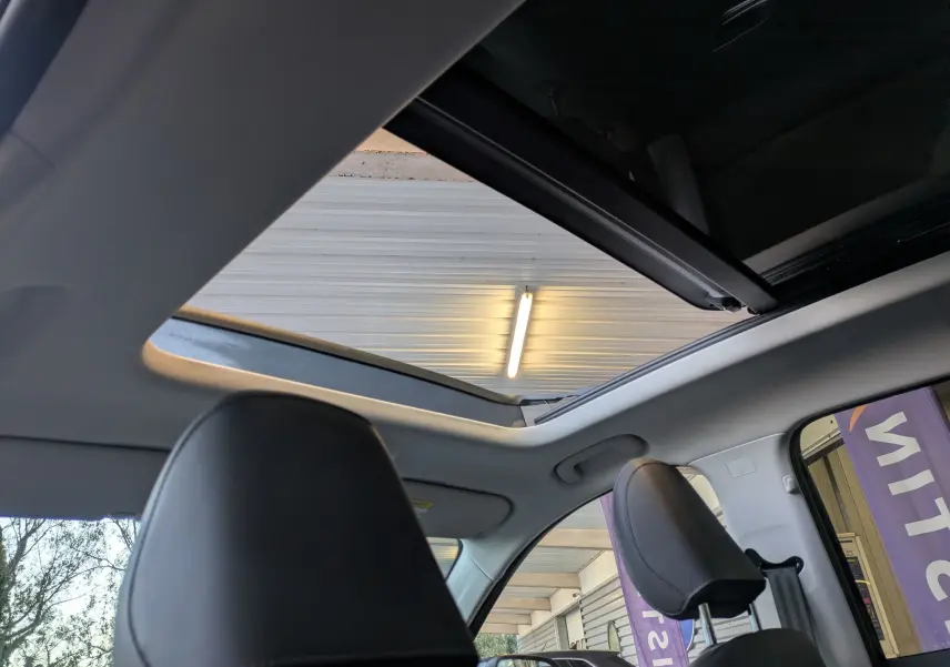 Vue intérieure du toit panoramique ouvert du MG MOTOR ZS noir, avec sièges avant en similicuir noir visibles.