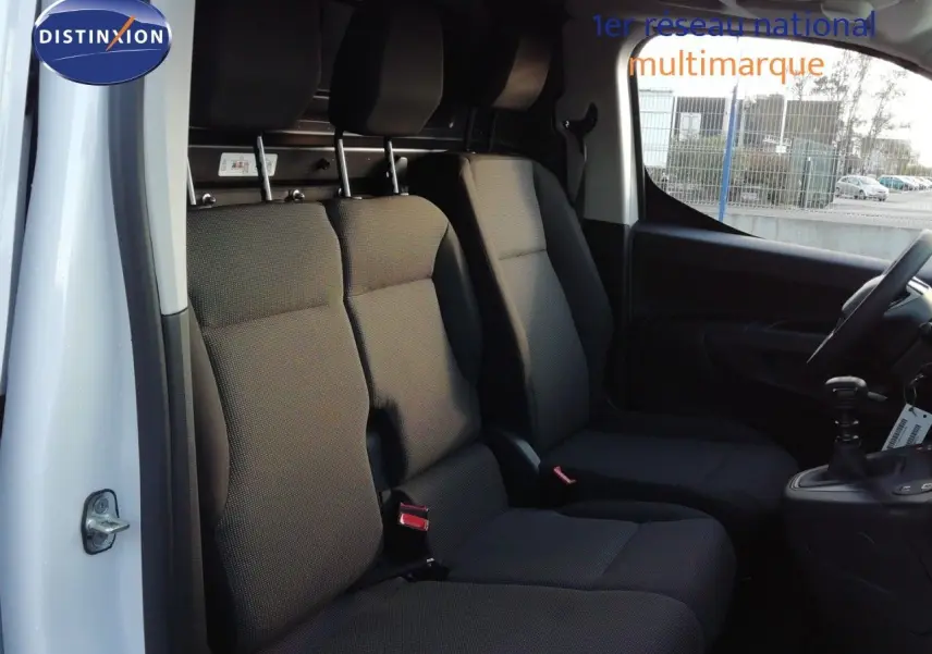 Vue intérieure côté conducteur du Peugeot Partner blanc Kaolin 2026, montrant les sièges avant en tissu gris foncé et la boîte manuelle.