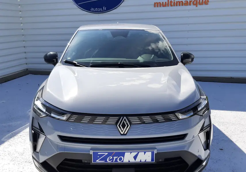 Vue frontale d'une Renault SYMBIOZ gris rafale 2024 avec calandre moderne et logo centré, stationnée devant un mur publicitaire.