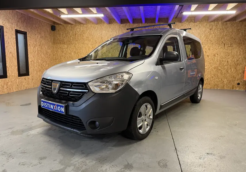 Vue 3/4 avant droite d'un Dacia Dokker gris 2019 avec calandre noire et barres de toit en intérieur bois.