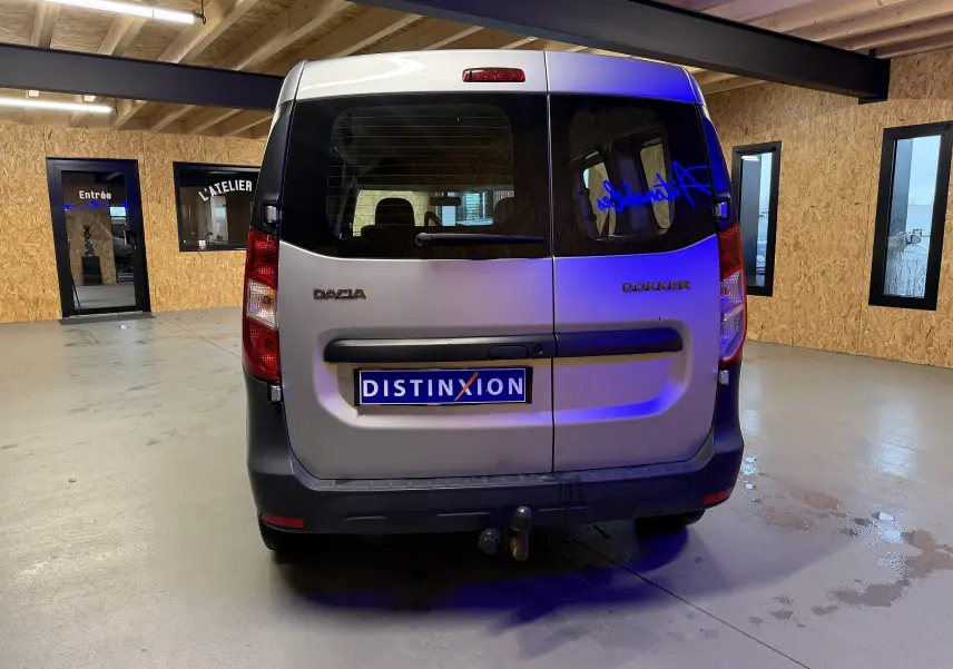 Vue arrière du Dacia Dokker gris 2019 avec portes battantes, attelage et plaque Distinxion visible en intérieur d'atelier.