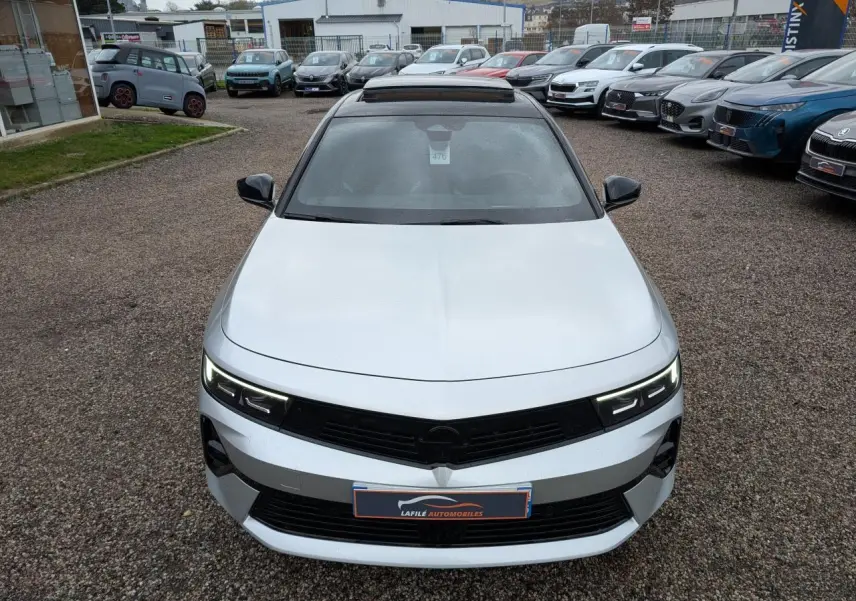 Vue avant d'une Opel Astra 2024 gris métallisé avec toit noir et phares LED allumés sur un parking.