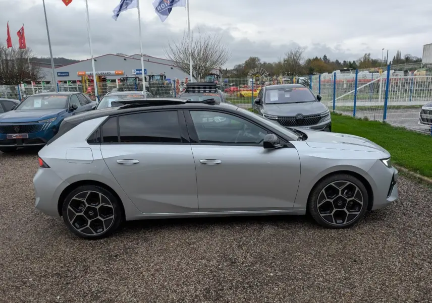 Vue de profil côté gauche d’une Opel Astra 2024 gris métallisé avec jantes au design hexagonal sur un parking extérieur.