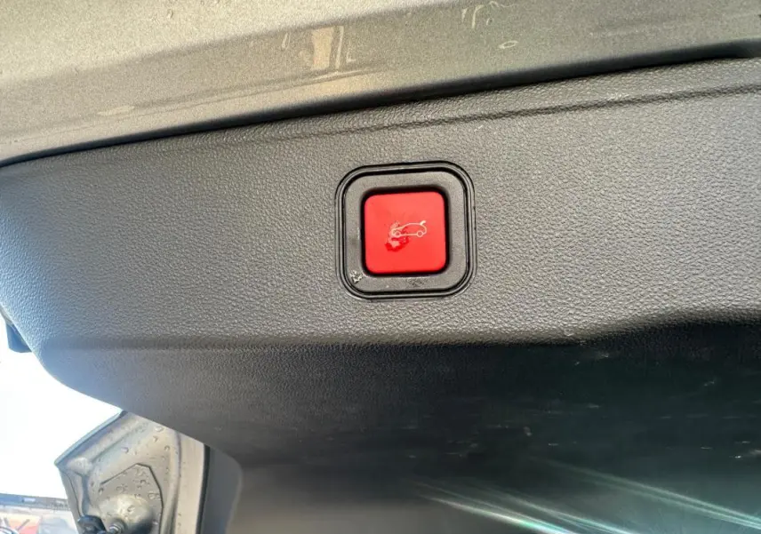 Gros plan sur le bouton rouge d'ouverture électrique du coffre, sous le hayon d'un Jeep Avenger gris foncé.