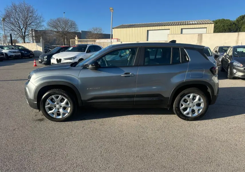 Vue de profil côté gauche d'un Jeep Avenger gris foncé avec jantes alliage 17 pouces sur un parking extérieur.