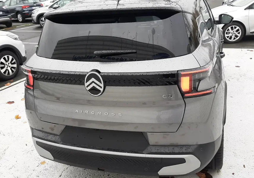 Vue arrière d'un Citroën C3 Aircross hybride gris avec toit noir, feux arrière allumés et détails noirs contrastants.