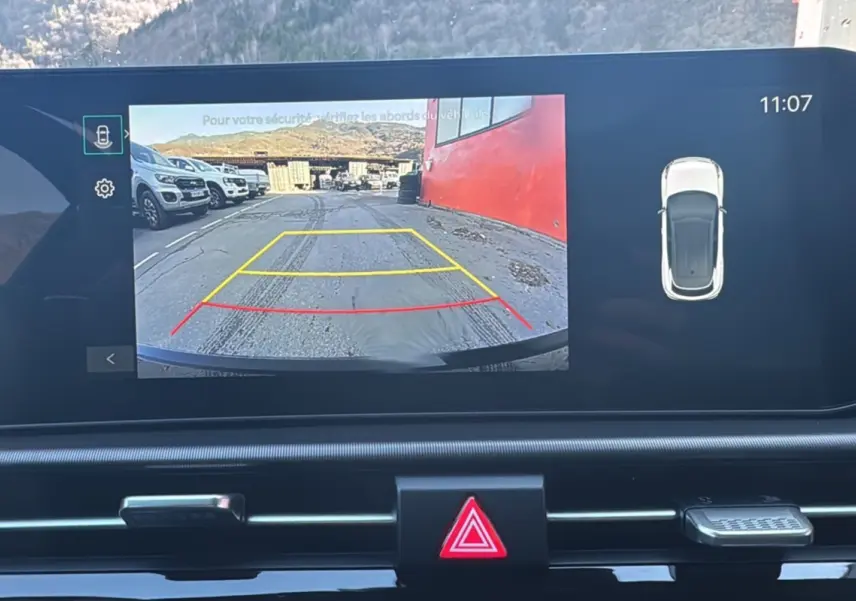 Écran multimédia du Kia Sportage 2026 montrant la caméra de recul avec vue arrière sur un parking et un mur rouge.