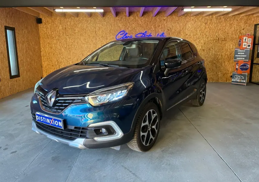 Renault Captur bleu 2017 en 3/4 avant droit, avec jantes alliage et calandre chromée, dans un garage intérieur.