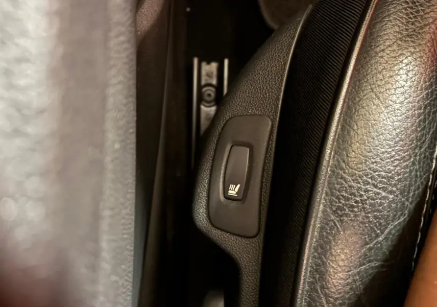Gros plan sur le bouton de siège chauffant noir dans l'habitacle du Renault Captur 1.5 DCI 90 Intens.