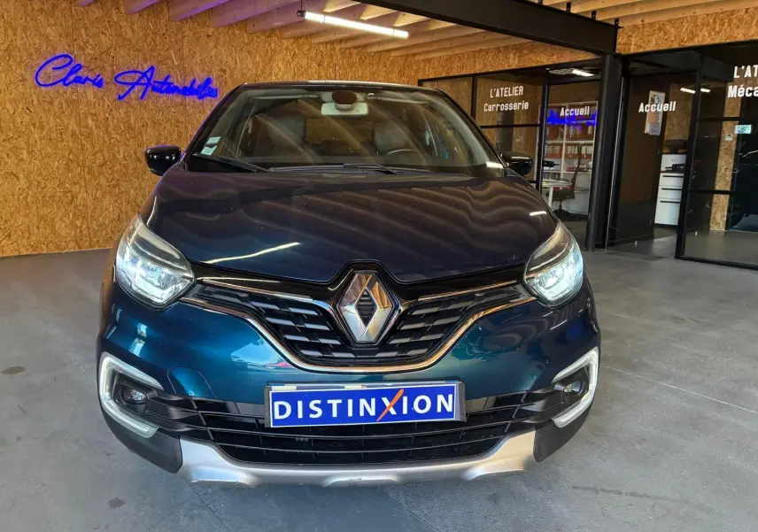 Vue de face du Renault Captur bleu 2017 avec calandre noire et plaque Distinxion dans un garage intérieur.