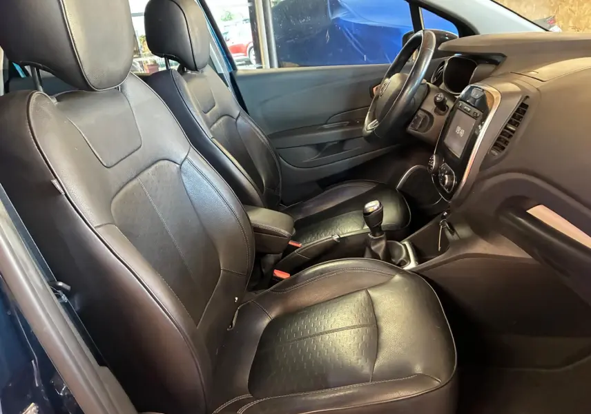 Vue intérieure côté gauche du Renault Captur bleu 2017, sièges avant en cuir noir et tableau de bord avec boîte manuelle.