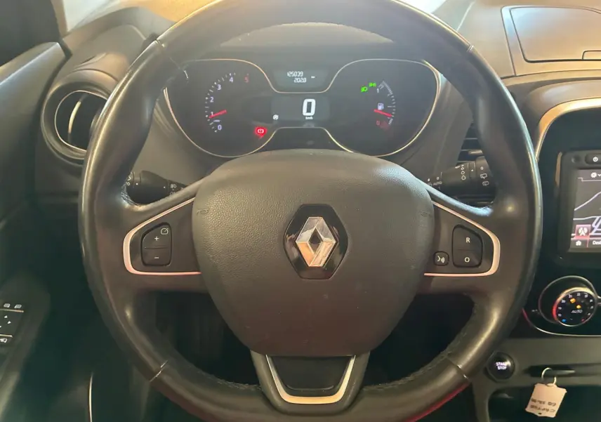 Vue intérieure centrée sur le volant noir avec logo Renault, tableau de bord numérique et commandes intégrées visibles.
