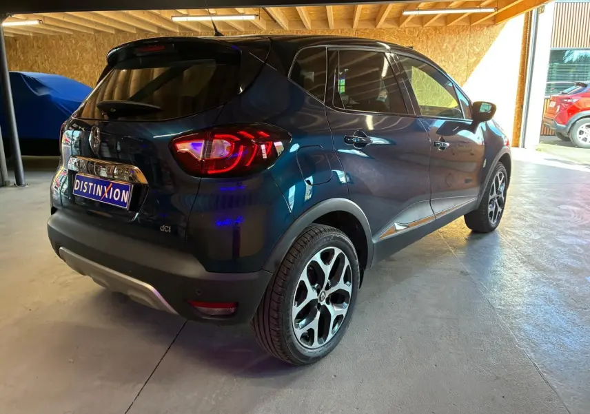 Vue 3/4 arrière droite d’un Renault Captur bleu 2017 avec jantes alliage et feux arrière allumés en intérieur.