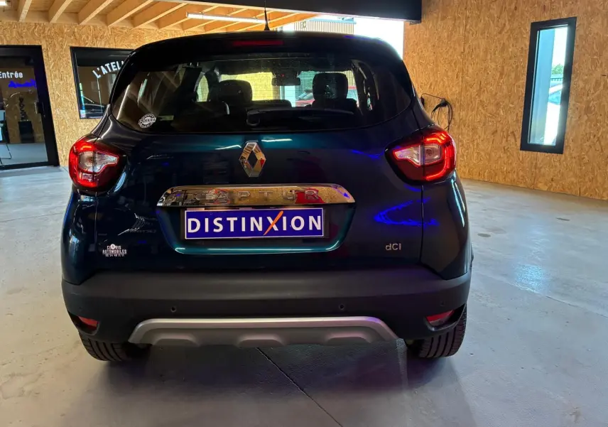 Vue arrière d'un Renault Captur bleu 2017 avec logo et plaque Distinxion dans un garage lumineux.