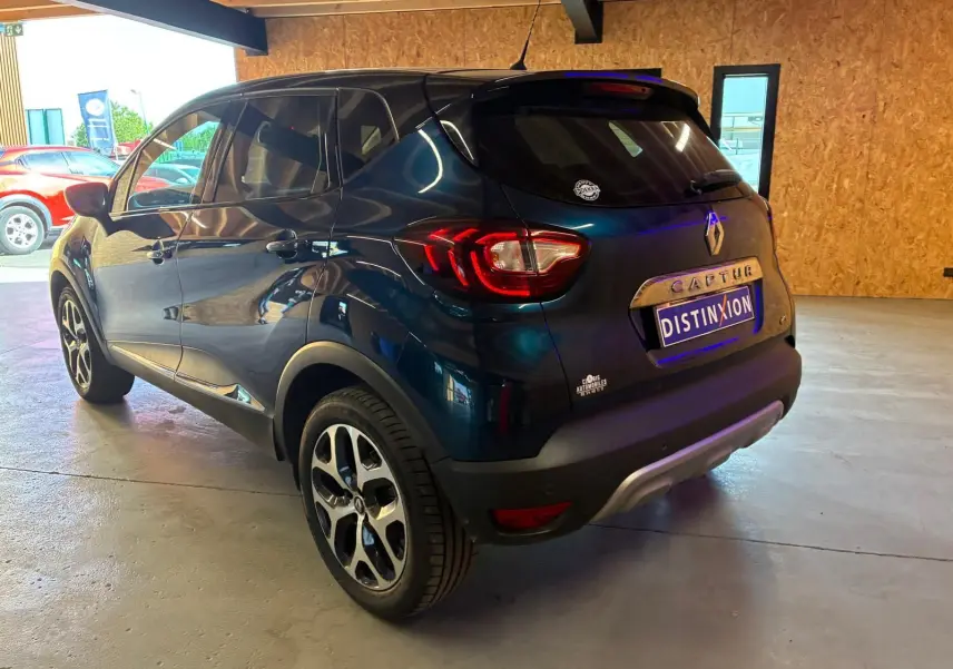 Renault Captur bleu 2017 en 3/4 arrière droit, avec feux arrière allumés et jantes alliage visibles.