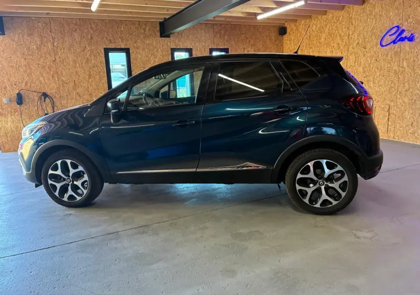 Vue de profil côté gauche d'un Renault Captur bleu 2017 garé en intérieur avec jantes alliage distinctives.
