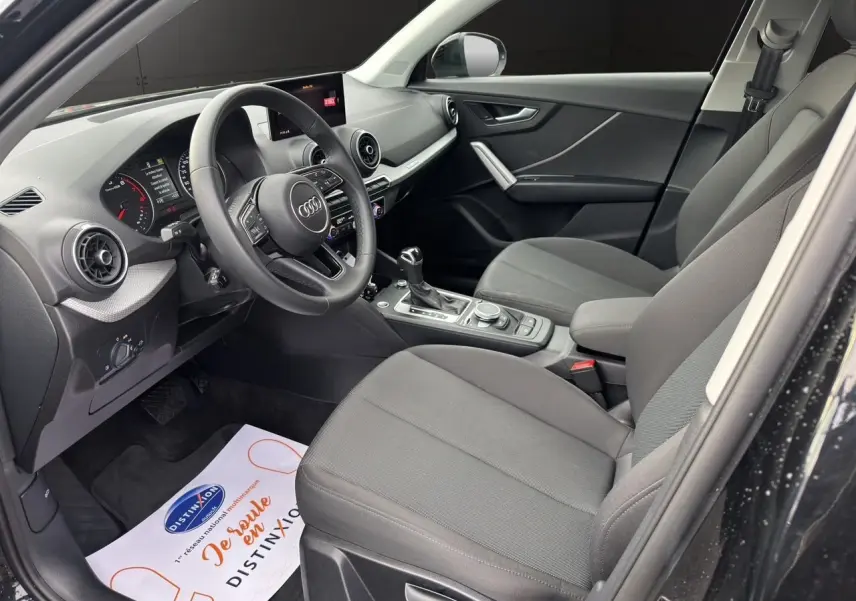 Intérieur avant droit d'Audi Q2 noir Mito 2023, sièges tissu gris, volant multifonction et console centrale avec levier automatique.
