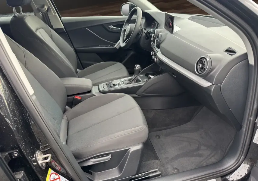 Intérieur côté passager d'un Audi Q2 noir Mito 2023, sièges tissu gris et tableau de bord moderne avec écran GPS.