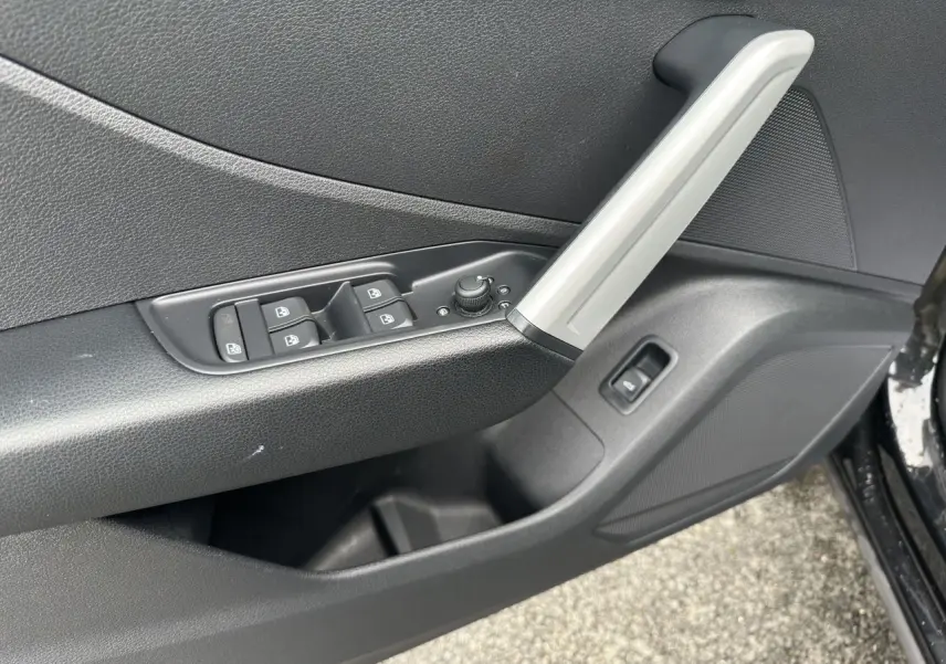 Gros plan sur la porte avant gauche noire de l'Audi Q2 2023, avec commandes des vitres et poignée argentée.