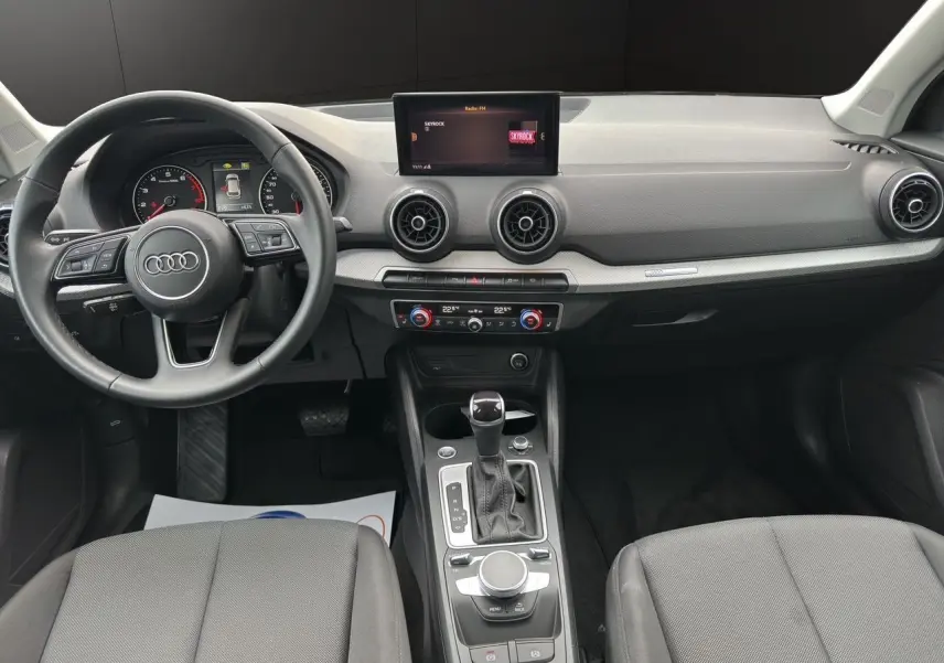 Vue intérieure avant de l'Audi Q2 35 TFSI S-Line 2023, tableau de bord noir avec écran central et commandes MMI visibles.