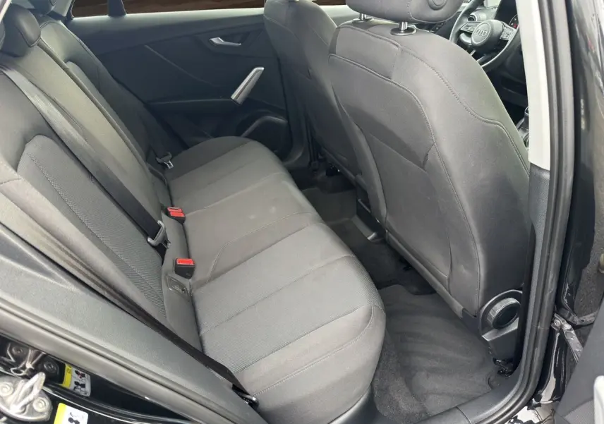 Vue intérieure côté arrière droit de l'Audi Q2 noir mito, montrant les sièges arrière en tissu et la porte ouverte.