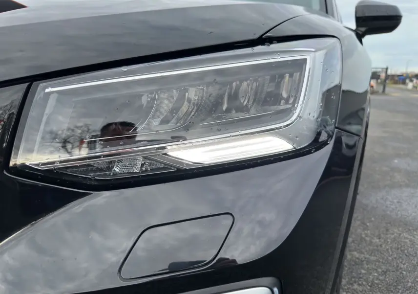 Gros plan sur le phare avant droit noir mito de l'Audi Q2 35 TFSI S-Line 2023 avec éclairage LED et capteur de lavage.