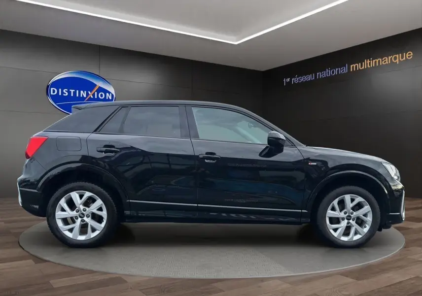 Audi Q2 noir mito vue de profil côté gauche, avec jantes alliage 7x17 et hayon motorisé visible en arrière-plan.