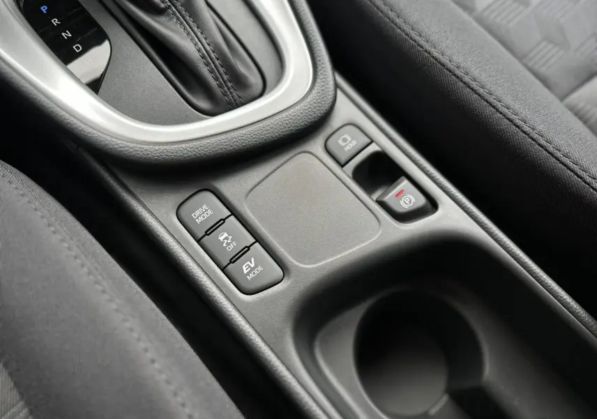 Gros plan sur la console centrale de la Toyota Yaris hybride 2025 avec boutons Drive Mode, frein électrique et sellerie tissu noir.